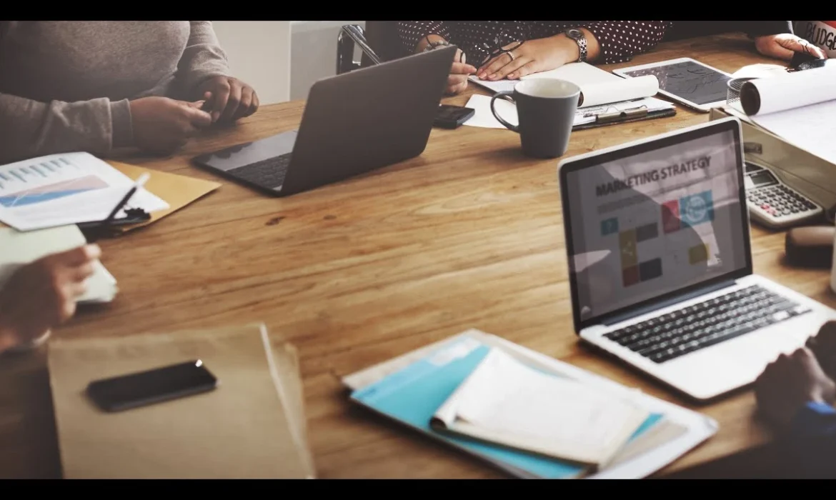 Marketing team collaborating at a wooden table with laptops and strategy documents.