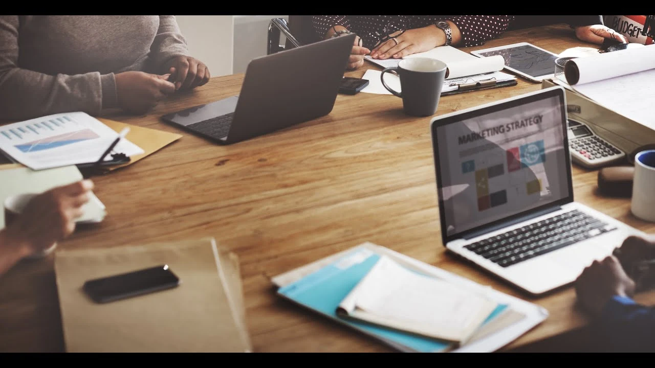 Marketing team collaborating at a wooden table with laptops and strategy documents.
