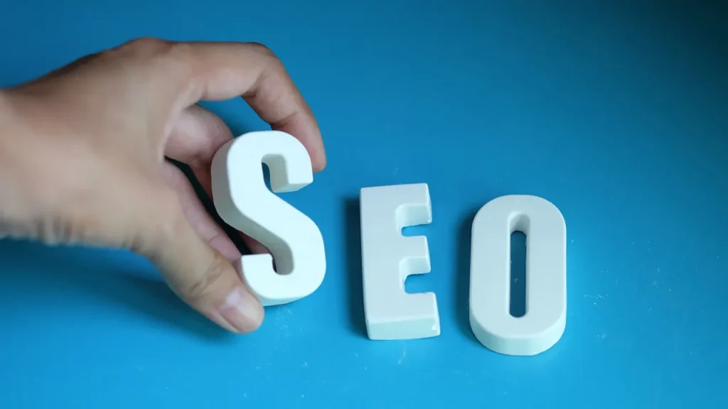 Hand holding the letter "S" beside "E" and "O" on a blue background, symbolizing SEO in a modern digital context.