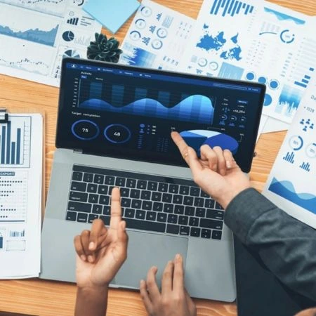 Two people analyzing charts on a laptop with financial reports on a desk.